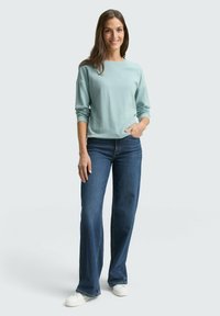 Himmelblaues, strukturiertes Langarmhemd kombiniert mit dunkelblauen Schlagjeans und weißen Sneakers. Einfaches, lässiges Outfit.