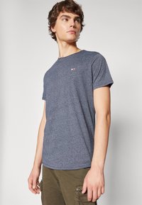 Marinblå t-shirt med kort ärm, med ett subtilt melerat mönster och logotypaccent på bröstet. Tillverkad av mjukt, strukturerat material.