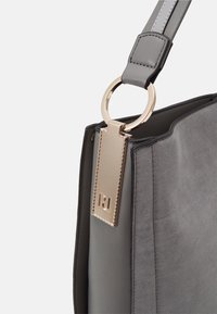 Sac à main gris avec une texture douce en daim et une sangle en cuir lisse. Comprend un anneau en or et une étiquette avec un détail de logo.