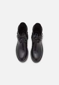 Botas de cuero negras hasta el tobillo con detalles florales, cremalleras laterales, punteras redondeadas y textura suave. La vista superior muestra los detalles y la artesanía.