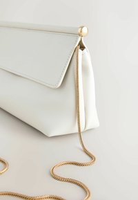 Pochette en cuir blanc avec un fermoir boule doré et une fine chaîne dorée reposant sur une surface lumineuse.
