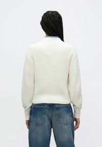 Ανοιχτό  κρεμ πουλόβερ με υφή, με ριμπ τελείωμα και μανσέτες, διαθέτοντας στρογγυλή λαιμόκοψη και χαμηλωμένους ώμους, σε συνδυασμό με μπλε τζιν παντελόνι.