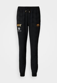 Pantalon de jogging noir avec un motif texturé, taille élastique avec cordon de serrage, accents dorés et logos imprimés sur le devant.