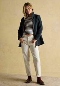 Námornícka fleecová bunda s vysokým golierom, nosená cez pruhovaný crop top, spárovaná s krémovými nohavicami a hnedými mokasínami s marhuľovými ponožkami.