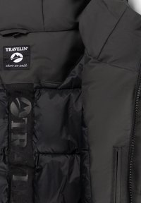 Zwart gewatteerd jack interieur met het label "TRAVELIN' waar we ook gaan" en geborduurd Thermolite-isolatie merk op de voering.