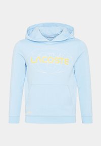 Ljusblå hoodie i bomullsblandning med en stor gul grafik "LACOSTE", känguruficka och vita rutmönster på ärmarna.
