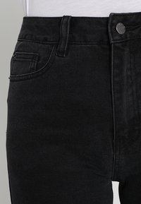 Svarta denimjeans med hög midja, en framficka med sömdetalj och knäppning med metallknapp. Slät yta.