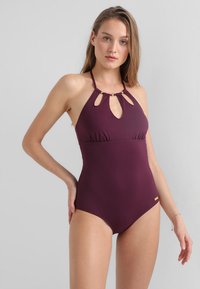 Maillot de bain une pièce bourgogne avec découpes en trou de serrure, bretelles halter et fronces discrètes à l'avant. Présente un petit accent en logo doré.