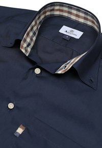 Camicia da uomo di colore blu navy con colletto in contrasto a quadri marroni e bianchi, parte anteriore in tinta unita, chiusura con bottoni e taschino sul petto con un accento decorativo.