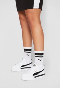 Baskets blanches à plateforme avec des rayures noires, semelles texturées et détails de logo. Associées à des chaussettes blanches avec des rayures noires et un logo.