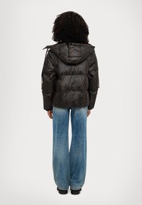Giacca imbottita marrone scuro con stampa animale a contrasto, dotata di cappuccio e polsini elasticizzati. Abbinata a jeans a gamba larga di colore azzurro chiaro.