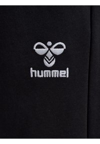 Sort stof med en broderet hvidt logo med et bi-design og ordet "hummel" nedenfor logoet. Glat tekstur uden mønstre.
