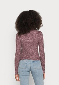 Camisola de mangas longas em tecido texturizado bordô, com um design ajustado, decote redondo e acabamento sem costuras, combinada com jeans azul claro.