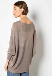 Hellbrauner übergroßer Strickpullover mit lockerem Sitz, weitem Ausschnitt und strukturierter Oberfläche. Lange Ärmel und ein dezentes Designelement auf der Rückseite.