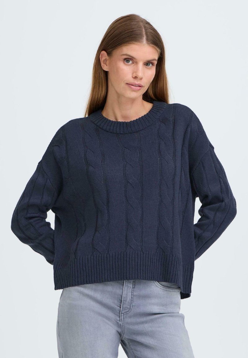 Marineblå kabelstrikket genser med ribbestrikket hals og kant. Løs passform med lange ermer og teksturerte mønstre gjennom stoffet.