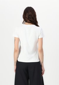 Camiseta blanca de manga corta con cuello redondo, fabricada en un material ligero y con un corte relajado. La parte trasera presenta un diseño liso y sin adornos.