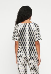 Haut à manches courtes en crème avec des motifs verticaux bleu marine, présentant un col bateau et une coupe décontractée, associé à un pantalon à motifs assortis.