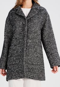 Cappotto a righe bianche e nere con colletto, maniche lunghe e due tasche frontali. Tessuto testurizzato con una vestibilità ampia e dritta.