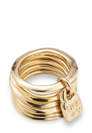 Anillos de oro apilados con una pequeña etiqueta en forma de corazón grabada con "UNO de 50" unida al anillo exterior.