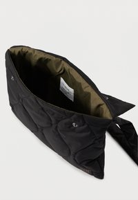 Crna vrećica s preklopnim uzorkom i maslinasto zelenim interijerom, koja sadrži dugmad za zatvaranje i oznaku unutra, dizajnirana za svestranu upotrebu.