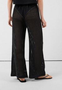 Pantalones negros de pierna ancha confeccionados en una tela ligera de punto abierto con un patrón rectangular, con una cintura alta y aberturas laterales.