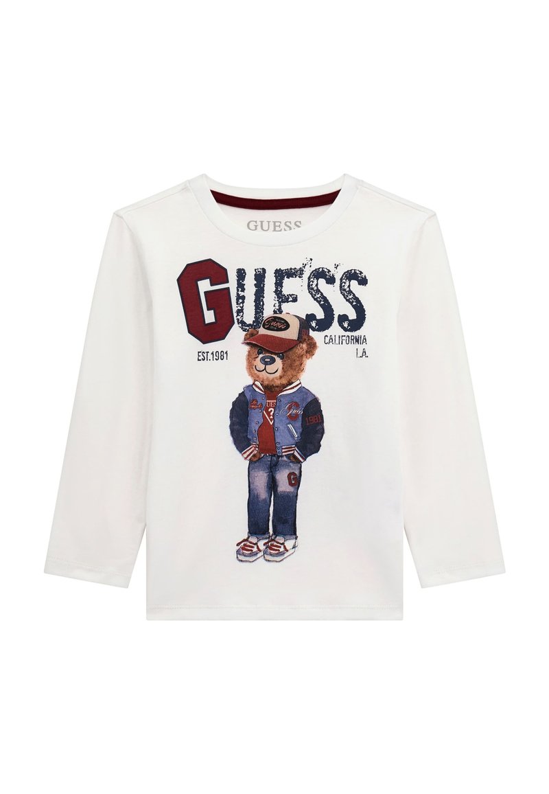 Weißes Langarm-T-Shirt mit einem Bärenmotiv, der eine Denim-Jacke, ein rotes Hemd, blaue Jeans und Sneaker trägt, sowie dem Aufdruck "GUESS" in fetten Buchstaben.