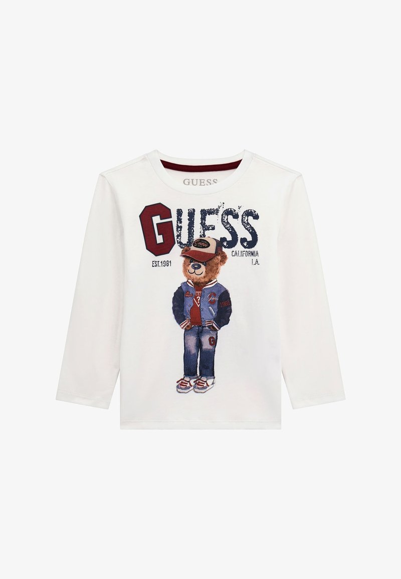 Weißes Langarm-T-Shirt mit einem Bärenmotiv, der eine Denim-Jacke, ein rotes Hemd, blaue Jeans und Sneaker trägt, sowie dem Aufdruck "GUESS" in fetten Buchstaben.