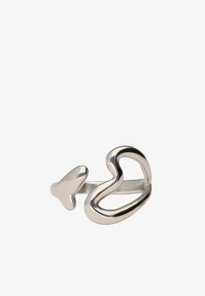 Anillo abierto de plata con un lazo en forma de corazón en un extremo y una pequeña punta de flecha en el otro, sobre un fondo blanco.