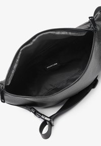 Borsa a tracolla in pelle nera con finitura testurizzata, chiusura con zip e foderatura in tessuto. All'interno presenta un'etichetta del marchio e un ampio scomparto.