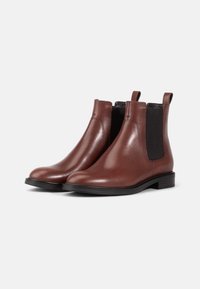Bottines Chelsea en cuir marron avec des panneaux latéraux élastiques, des pointes arrondies et des languettes. Présente une finition lisse et un talon noir contrastant.