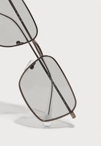 Ochelari de soare cu ramă metalică, cu lentile gri, formă rectangulară, pernuțe nazale transparente și detalii gravate pe templul interior.