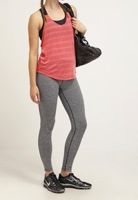 Szare legginsy z czarnymi bocznymi paskami, zestawione z czerwonym tank topem w paski. Czarne buty sportowe i czarna torba na ramię dopełniają całość.