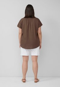 Bruin kortärmlig top met een losse pasvorm, gecombineerd met witte opgerolde korte broek. De stof lijkt lichtgewicht met een gladde textuur.