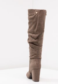 Botte molletière décontractée en daim doux, marron, avec un talon épais. Présente un petit accent circulaire près du haut et une texture lisse.