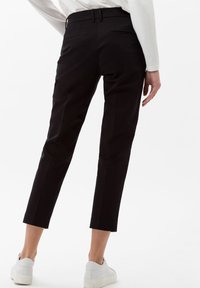 Pantaloni neri corti realizzati in un tessuto liscio, con vita aderente, tasche posteriori e orli arrotolati, abbinati a sneaker bianche.