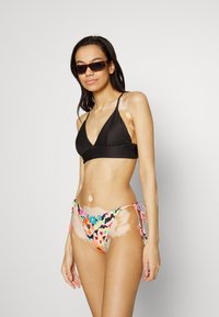 Top de bikini preto com textura em rèsted e design em V. Parte de baixo de bikini com estampa floral e laterais com atilhos em cores vibrantes. Óculos de sol com estampado de tartaruga.
