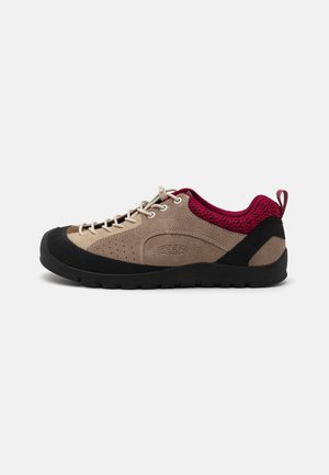 Scarpa con tomaia in suede beige, suola in gomma nera, dettagli in rete rosa e lacci grigi. Presenta perforazioni per la traspirabilità e una linguetta per facilitare l'indossamento.