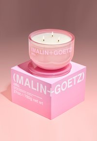 Drei-Docht-Kerze in einem durchsichtigen rosa Glasbehälter, platziert auf einer passenden rosa Box mit weißem Text, einschließlich Marken- und Gewichtsangaben.