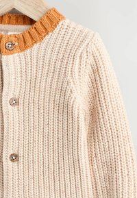 Stickad cardigan i krämfärg med en strukturerad yta, med en varm orange ribbad krage och stängning med träknapp.