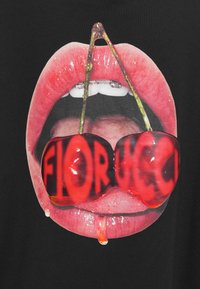 Lábios vermelhos brilhantes com a boca aberta segurando duas cerejas com hastes, com reflexos vermelhos formando a palavra "FIORUCCI" nas cerejas.