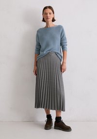 Jasnoniebieski sweter z dzianiny, szara spódnica plisowana i ciemnobrązowe sznurowane buty. Ubranie ma teksturowany materiał i luźny krój.