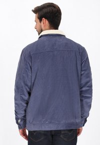 Tengerészkék kordbársony dzseki krém színű műszőrmeghasítással, hosszú ujjak és gombbal záródó mandzsetták, laza szabással és texturált anyaggal.