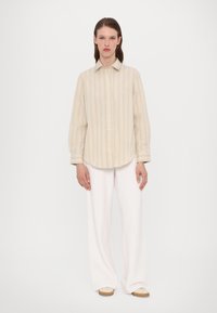 Rutet knapperup skjorte i beige og krem, lange ermer, buet falm. Kombinert med hvite vide bukser og beige slip-on sko.