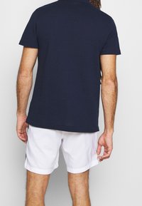 Tmavě modré polo tričko s krátkým rukávem z bavlny, kombinované s bílými plavkovými šortkami. Pohodlný střih s jednoduchým designem a jednobarevným provedením.