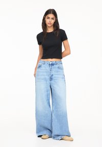 Zwarte cropped t-shirt gecombineerd met lichtblauwe spijkerbroek met wijde pijpen; soepele textuur, ceintuur in de taille en een relaxed fit.