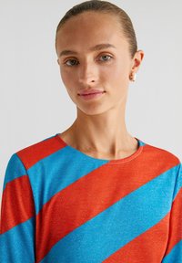 Langarmtop met gedurfde diagonale strepen in rood en blauw met een subtiele glans. Soepele textuur en een ronde halslijn.