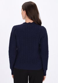 Navyblauer Strickpullover mit gerippter Textur, rundem Ausschnitt und langen Ärmeln. Besitzt einen taillierten Saum und ein strukturiertes Muster auf der Rückseite.