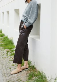 Grå stickad omslagskofta med en knytdetalj, i kombination med högmidjade bruna läderbyxor och vävda beigea slipskor.