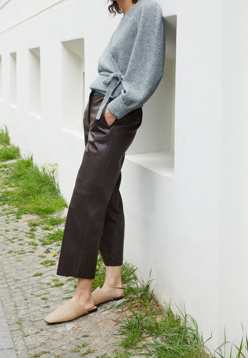 Grå stickad omslagskofta med en knytdetalj, i kombination med högmidjade bruna läderbyxor och vävda beigea slipskor.