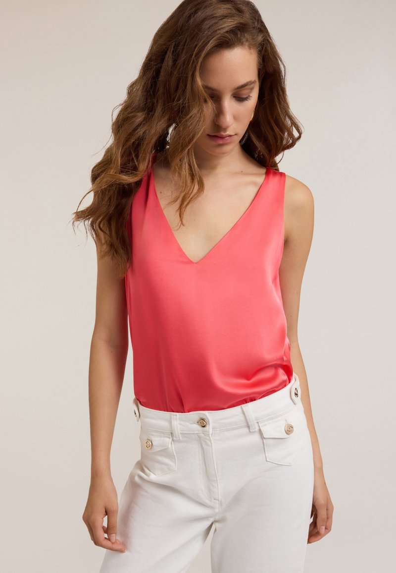 Top de satén color coral con diseño de escote en V, combinado con pantalones blancos de talle alto que cuentan con detalles de botones dorados. Textura suave.